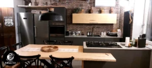 Cucina stile industrial con mattoni a vista, penisola con piano in legno grezzo e bancone, ristrutturazione Grosseto.