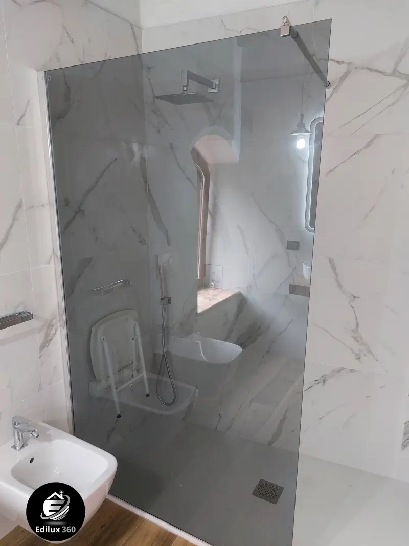 Dettaglio della doccia con ampio pannello in vetro e rivestimento in piastrelle effetto marmo a tutta altezza.