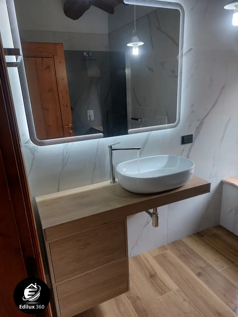 Lavabo ovale da appoggio su mobile sospeso in legno scuro con specchio a LED in bagno elegante.