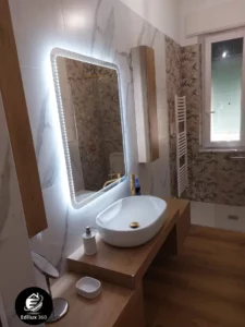 Lavabo da appoggio moderno su mobile in legno chiaro con specchio retroilluminato a LED in bagno ristrutturato.