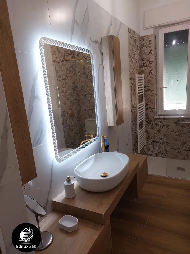 Lavabo da appoggio moderno su mobile in legno chiaro con specchio retroilluminato a LED in bagno ristrutturato.